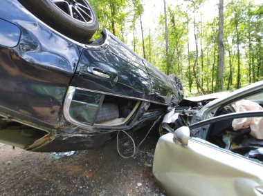 Çarpışmaya giren iki hasarlı araba, bir araç yan yatmış, etrafı ağaçlarla çevrili..