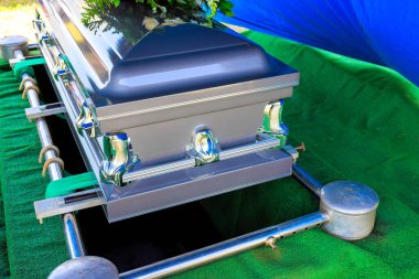 Tabut dikkatlice mezara indirilir. Cenaze töreni sırasında yeşil çim çiçekleriyle çevrilidir.