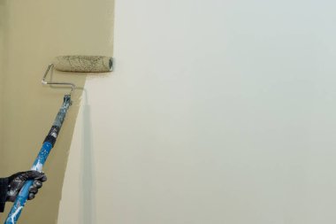 Müteahhit, içerideki odayı yenilerken duvara hafif boya uygulamak için boya silindiri kullanıyor..