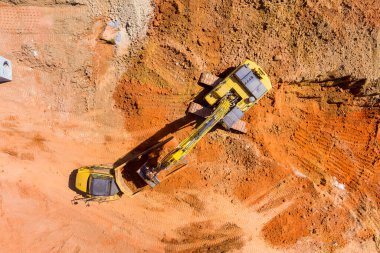 İnşaat alanında yer kazan ağır makineler ve onları çevreleyen kırmızımsı toprak..