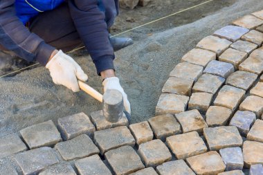 İşçiler yol üzerinde kaldırım taşlarını titizlikle düzenliyor, iş günlerinde ustalık gösteriyorlar.