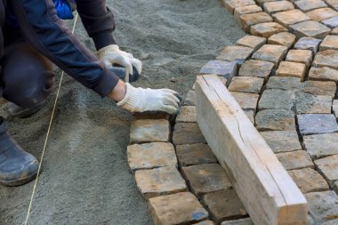 İnşaat işçisi iş gününün altındaki kumlu temele kaldırım taşlarını dikkatlice yerleştiriyor.