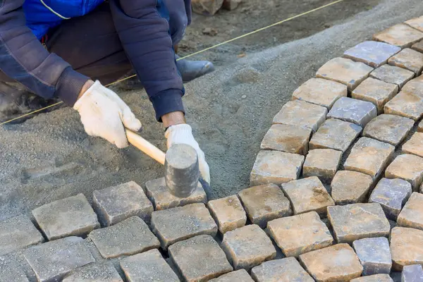 İşçiler yol üzerinde kaldırım taşlarını titizlikle düzenliyor, iş günlerinde ustalık gösteriyorlar.