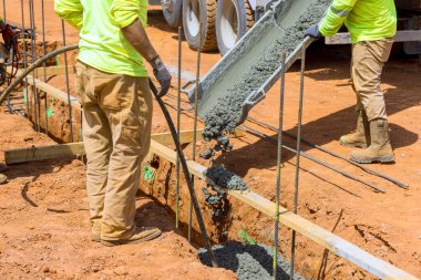 Parlak giysili işçiler inşaat alanındaki hendeğe gündüz vakti beton dökerler.