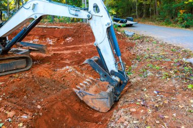 Ağır makineler gün içinde ağaçlarla çevrili çakıl yolunun yakınındaki kırmızı çamurda çukur kazıyor.