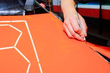 Yetenekli el, araba servisinin içindeki el yapımı bıçağı kullanarak canlı turuncu malzemeyi titizlikle kesiyor.