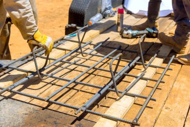 İşçiler, inşaat iş günü için hazırlanırken ahşap platformda demiri şekillendiriyorlar.