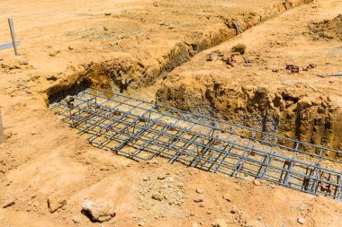 Çalışma saatleri boyunca inşaat sahasında beton temeller için kazılmış alan demiri döşeniyor.