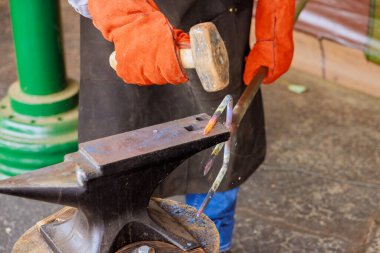 Yetenekli demirci örse sıcak metal çakıyor. Bahçe çatalı yapımı sırasında geleneksel zanaatkarlık sergiliyor.
