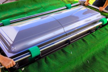 Tabut çimenli bir alanda, resmi bir cenaze sahnesinde kayıp yansıması hissi uyandırıyor..