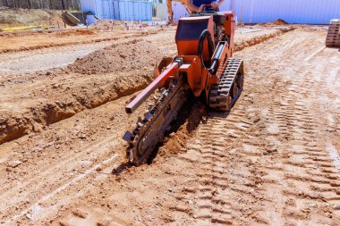 İnşaat ekibi inşaat alanındaki elektrik hatları için derin hendek kazma makinesi kullanıyor.