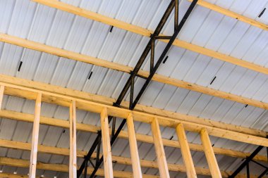 Parlak ışıklandırılmış iç mekan, inşaat aşamasındaki ahşap çerçeve metalini açık tavanlı destekliyor..