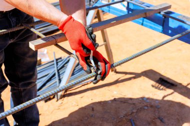 Eldivenli işçiler çelik inşaat iskeleti inşa ederken metal demiri penseyle kavrıyor