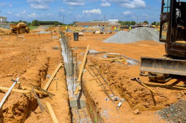 İşçiler büyük inşaat sahasında çalışma gününde makinelerle temel inşa ediyorlar.