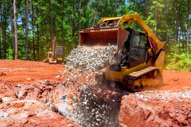 İnşaat traktörü ekipmanları taşları ormanlık alandaki siperlere boşaltıyor.