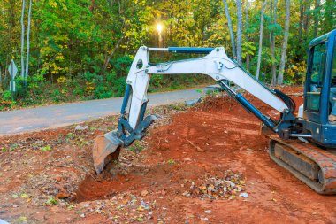 Bir kazıcı inşaat alanında ağaçlarla çakıl yolu boyunca toprak siper kazıyor.
