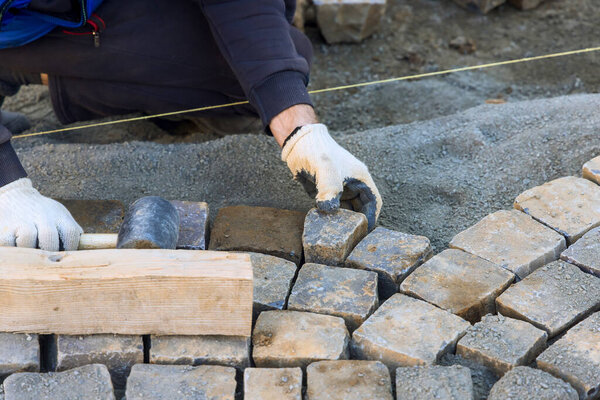 Опытный рабочий тщательно позиционирует каменные кирпичи для дорожки, обеспечивая их надежное равномерное размещение в рабочий день..