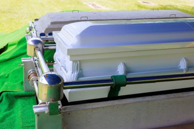 Beyaz tabut yeşil bir defin bezine dayanır. Açık hava düzeniyle çevrili. Bu da vedalaşma anını gösterir..