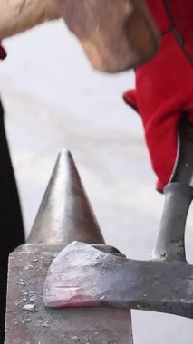 Yetenekli zanaatkar şekilleri koruyucu eldiven giyerken örsün üzerinde parlayan baltalar yapıyor..