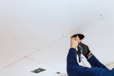 Kalifiye işçiler, konut alanındaki merdiven üzerinde dururken aletlerle tavan boşluğunu tamir ediyor..