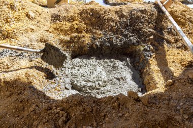 İşçiler inşaat alanında kum kürekleriyle büyük bir delikte taze beton hazırlıyorlar..