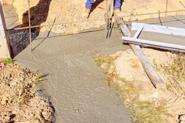 İşçiler inşaat alanındaki temel kalıplarına ıslak beton döküyorlar.