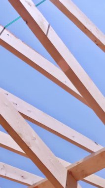 İnşaat sırasında ahşap çatı kirişlerine ve yapısal iskelete yakın plan, mavi gökyüzü arka planına karşı karmaşık kiriş bağlantılarını gösteriyor.