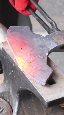 Demirci, balta yapımı sırasında ustaca parlayan metal parçasını çekiçle şekillendirir.