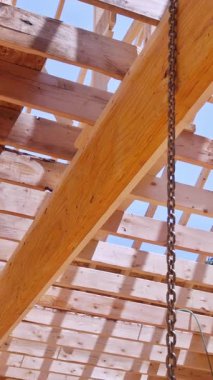 Mimari ahşap çatı çerçevesinin kesişen kirişlerle yakın görüntüsü, inşaat sürecini ve mavi gökyüzüne karşı yapısal detayları gösteriyor