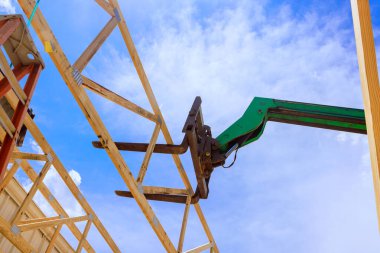 İnşaat alanı forklift telsizcisi, açık mavi gökyüzünün altına tahta kirişleri kaldırıyor..