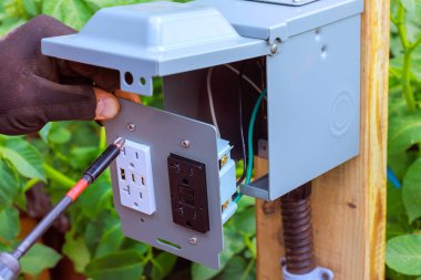 Teknisyen, ahşap direğe monte edilmiş dış elektrik prizi USB portlarına kablo bağlıyor.