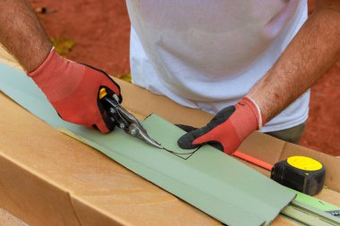 Kalifiye işçi, ahşap yüzeyde doğru ölçüm yaparken yeşil kaplama kesmek için makas kullanır.