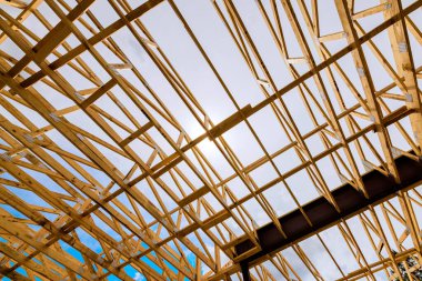 İşçiler çatı için ahşap kirişleri birleştirirken, güneş ışığı çerçeve boşluklarından akıyor.