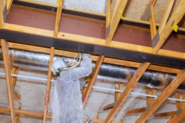 İnşaat işçisi ustalıkla ahşap kirişlerin yapısına köpük yalıtım spreyi yerleştiriyor.