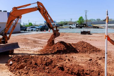Kazıcı işlek inşaat sahasında aktif olarak kazı yapıyor. Yakınlardaki birkaç araç endüstriyel gelişimi sağlıyor.