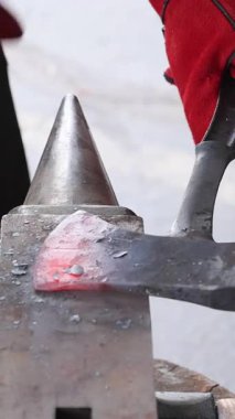 Bir zanaatkar koruyucu eldiven giyerken örsün üzerinde parlayan balta şekilleri yapar..