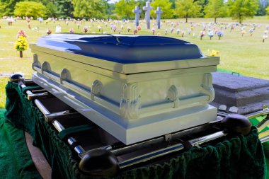 Tabut mezarlıkta sergileniyor. Çiçek açan mezar taşlarıyla çevrili.