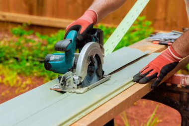 İşçi, ev geliştirme çabalarında vinil ön kaplamayı kesmek için dairesel testere kullanıyor.