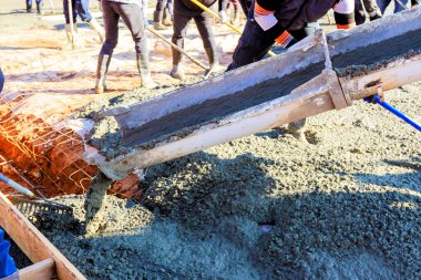 İnşaat işçileri çalışma gününde temel döşemeleri hazırlarken beton karışımı döküyorlar..
