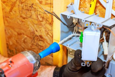 Teknisyen ahşap duvarda bir elektrik düğmesi kuruyor. Aletlerle el işi yapıyor..