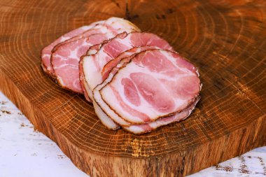 Tahtaya yerleştirilmiş ince tütsülenmiş et dilimleri yumuşak ışık altında zengin renk dokuları sergiliyor..