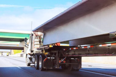 Ağır kamyon otoyolda bir üst geçidin altından geçerken büyük miktarda beton kiriş taşıyor..