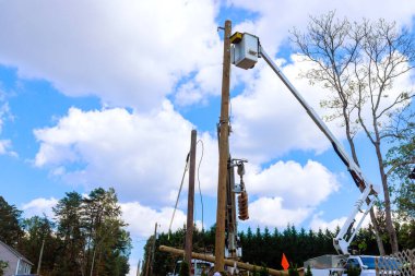 Elektrik teknisyeni, elektrik direğindeki ekipmanları tamir etmek için iş günü kaldırma platformunu kullanıyor.