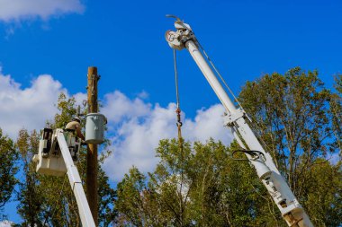 Havadaki işçiler, çevresindeki ağaçlarla çevrili açık mavi gökyüzünün altındaki elektrik hatlarını tamir ediyorlar..