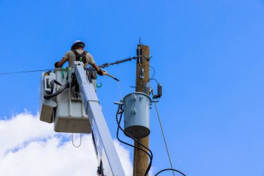 Elektrik işçisi, parlak güneş ışığı altında kova kamyonun tepesindeki elektrikli ekipmanları inceliyor..