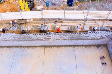 Birkaç inşaat işçisi yoğun inşaat sahasına duvar örmek için beton bloklar döşüyorlar..
