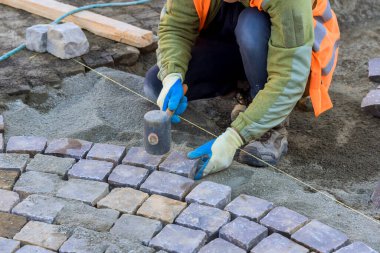 İşçi kaldırım taşlarını dikkatlice yerleştirmek için çekiç kullanır..