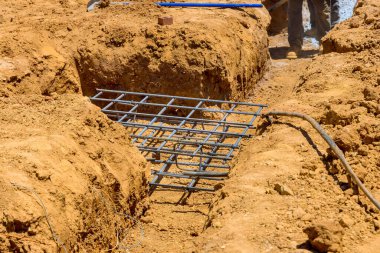İşçiler inşaat sırasında inşaat sahasında toprak dolu bir sipere demirleme ızgarası döşenmiş sağlam bir temel hazırlıyorlar.
