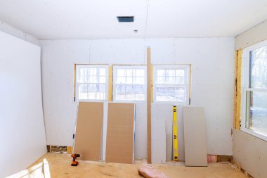 İşçiler alçıpan çarşaflarını birden fazla pencereli, ahşap kirişli iyi aydınlatılmış odada hazırlıyorlar..