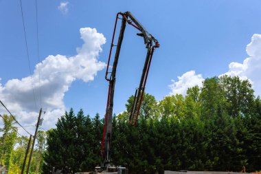 İşçiler arka planda inşaat alanı hazırlarken beton pompa kamyonu parlak mavi gökyüzüne karşı dik duruyor..